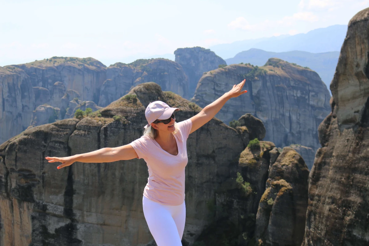 meteory grecja - Rita z rozłożonymi rękami na tle klasztorów Meteorów w Grecji, uśmiechnięta i pełna radości.