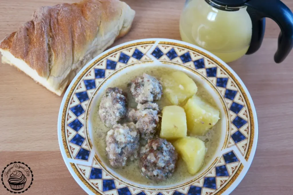Giouvarlakia avgolemono – tradycyjne greckie klopsiki w sosie cytrynowym z wołowiną i ryżem, podane na talerzu obok chleba i soku z cytryny
